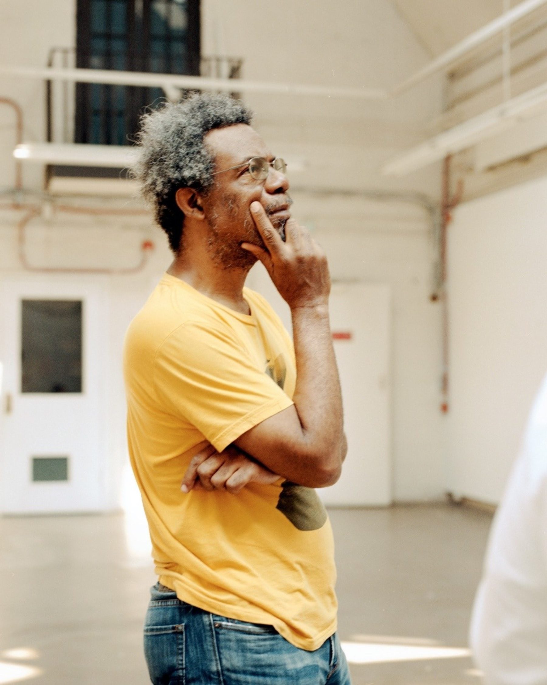 Artist Pope.L. wearing a yellow shirt and facing sideways.